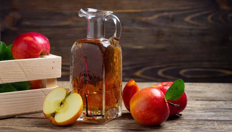 botella de vinagre en mesa rodeada de manzanas